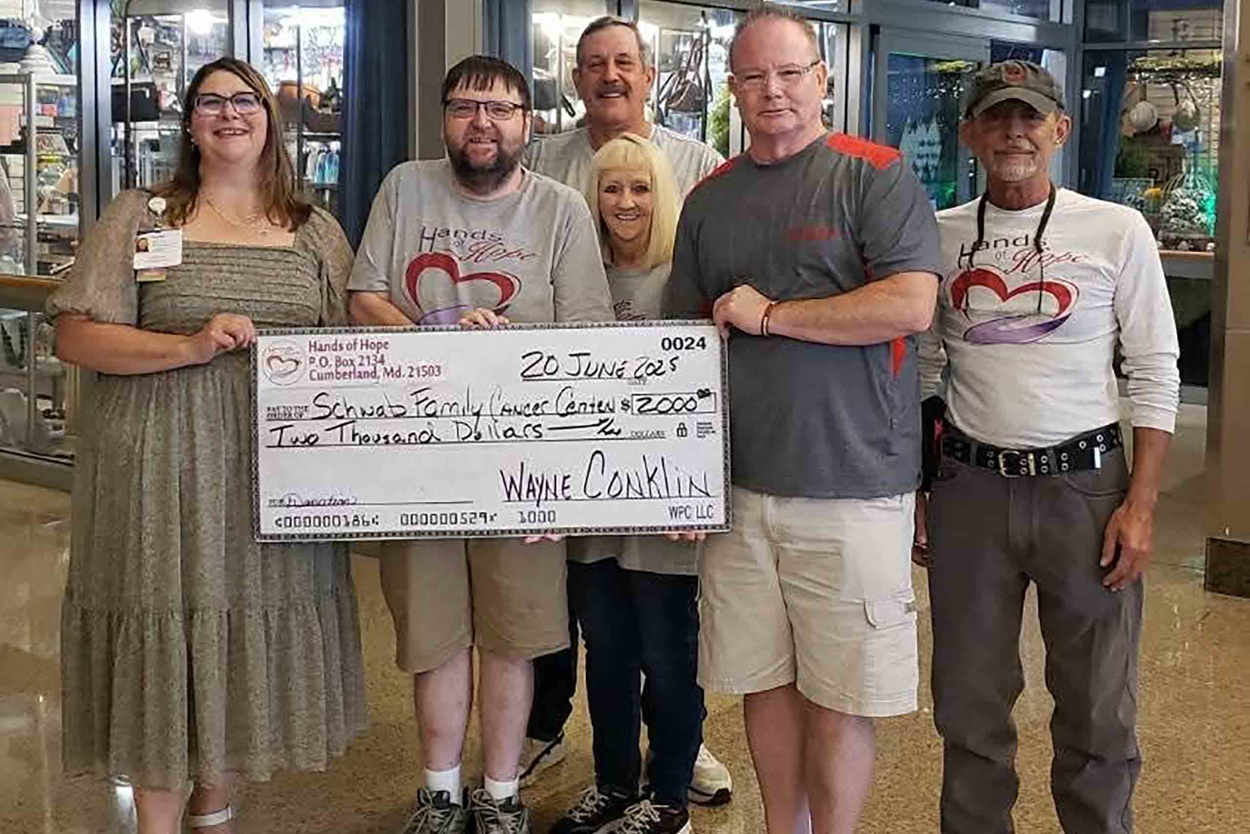 Six people pose together while holding a $2,000 ceremonial check from Hands of Hope made out to the Schwab Family Cancer Cente